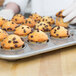 A hand holding a Chicago Metallic mini muffin pan filled with muffins.