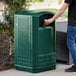 A person putting a can into a Rubbermaid dark green Plaza outdoor trash container.