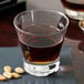 An Arcoroc Shetland rocks glass filled with liquid next to a bowl of peanuts on a table.