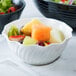 A close-up of a white Cambro swirl bowl filled with fruit salad.