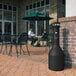 A Rubbermaid black cylinder shaped cigarette receptacle on a brick patio.