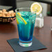 A highball glass with blue liquid and a lemon slice on a napkin.