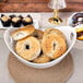 A white porcelain bowl with cut outs holding bagels on a table.