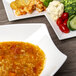 A white rectangular porcelain bowl filled with soup, rice, and vegetables on a table.