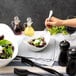 A hand holding a fork in a white porcelain cradle bowl filled with salad.