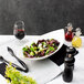 A salad in a 10 Strawberry Street white porcelain banana bowl next to a glass of red wine.