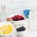 A bowl of blueberries, raspberries, and blackberries on a counter with a bowl of sliced lemons.