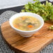 A 10 Strawberry Street Whittier white porcelain footed bowl of soup on a wooden surface.