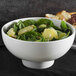 A white ribbed porcelain bowl filled with spinach and orange slices on a table.