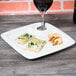 A 10 Strawberry Street Whittier white porcelain appetizer plate with food and a wine glass on it.