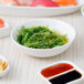 A white porcelain sauce dish filled with red sauce on a table with other food.
