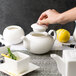 A person pouring tea into a white 10 Strawberry Street Whittier teapot.