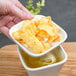 A hand holding a white porcelain bowl with a piece of food in it.