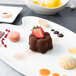 A white porcelain easel holding a china platter with a chocolate cake, strawberries and a lemon.