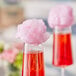 A close-up of a glass with pink liquid and a pink cotton candy on top.