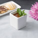 A 10 Strawberry Street white square porcelain bowl with a pastry inside on a table with a cup of liquid and mint leaves.