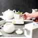 A person using a 10 Strawberry Street White Porcelain Tid Bit Tray to pour tea into a bowl of fruit.