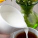 A person pouring milk into a white 10 Strawberry Street porcelain milk cup.