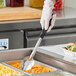 A person using a Vollrath 3-sided solid basting spoon to serve food from a white tray.