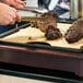 A person cutting meat on a Cal-Mil replacement cutting board.