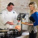 A man and woman serving food from a Vollrath Contoured Carving Station.