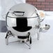 A Vollrath stainless steel chafing dish with a silver lid on a table.
