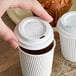 A hand putting a white Choice paper lid on a cup of coffee.