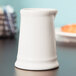 A white Tuxton china creamer on a table.