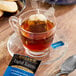 A glass cup of Bigelow English Teatime tea with a tea bag on a saucer and a spoon.