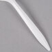 A white plastic Dart teaspoon on a gray surface.