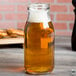 An American Metalcraft glass milk bottle filled with a yellow liquid on a table.