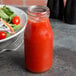 An American Metalcraft glass milk bottle filled with red liquid next to a bowl of salad.