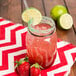 An American Metalcraft condiment mason jar filled with a red drink and a straw with limes next to it.