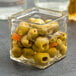 An American Metalcraft square glass condiment jar filled with green olives.