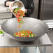 A man pouring vegetables into a Town hand hammered Cantonese wok.