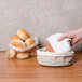 A hand lining an American Metalcraft Cream and Gray Canvas Bread Basket with a white towel.