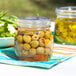 A table with a jar of green olives and a bowl of salad.