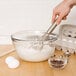 A hand whisking a bowl of flour and eggs with an Anchor Hocking glass bowl.