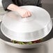 A hand holds a Town aluminum wok cover over a bowl of vegetables.