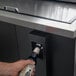 A person pouring a bottle of beer into a Continental black horizontal bottle cooler on a bar counter.