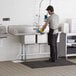 A man washing dishes in a Regency 3 compartment sink with a left drainboard.