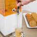 A hand pouring liquid from a stainless steel Cal-Mil beverage dispenser into a glass.