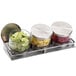 A Cal-Mil stainless steel display holding three glass jars with metal lids filled with limes.