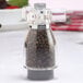 A Chef Specialties acrylic pepper mill with black peppercorns inside.