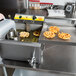 A man using a Carnival King funnel cake fryer to pour batter into hot oil on a counter.