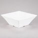 A white square Tablecraft melamine bowl with a corner on a gray surface.