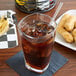 A glass of ice tea with a straw next to a plate of chicken nuggets.