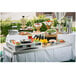 A Tablecraft brushed stainless steel cover on a table with food and a water dispenser.