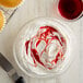 A bowl of white whipped cream with red swirls next to a knife.