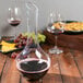 A Chef & Sommelier glass decanter with red wine on a table with food.